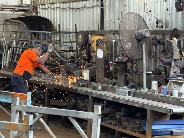 Grinder throwing sparks over a bench of angle and channel offcuts